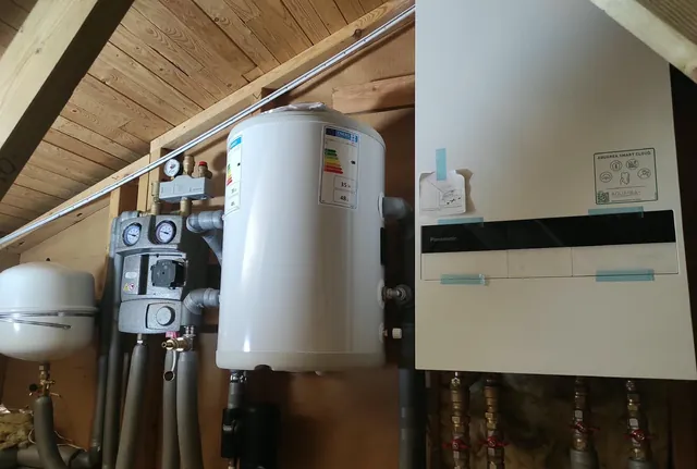 Technikwand im Spitzboden eines Holzhauses: Pumpengruppe, Pufferspeicher und Wärmepumpen-Innengerät nebeneinander montiert